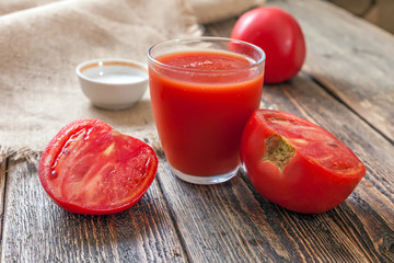 Tomato juice in a glass and slices of a tomato on a wooden table
