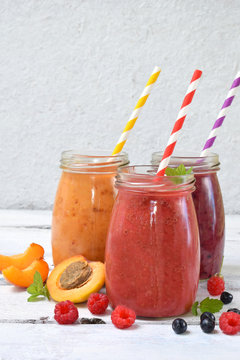 Orange, red and purple healthy smoothies of fresh ingredients - bananas, apricots, raspberries and blueberries on a light background. Copy space