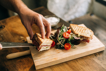 Man prepares lunch, serves grilled bread sandwich snack on top of wooden cutting board, with side of green salad, healthy alternative to burgers and grease - Powered by Adobe