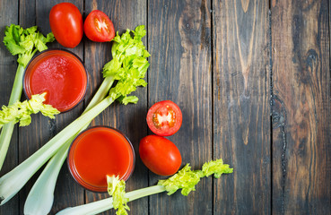 Tomato juice in glass with celery, tomato on wood background, closeup