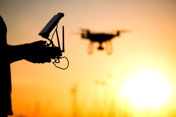 Naklejka na ściany i meble Young man operating of flying drone the setting sun