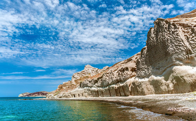 Fototapeta na wymiar Views of the rocky coastline of the Greek island of Thira or Santorini and blue sky with spindrift clouds.