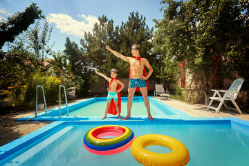 Father and son in suits of superheroes in the pool in the summer.