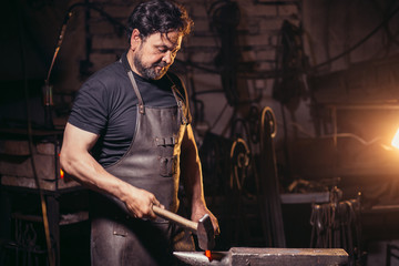 blacksmith manually forging the molten metal on the anvil in smithy with spark fireworks
