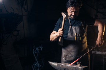 Senior blacksmith forging the molten metal on the anvil in smithy.