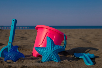 Children's joys on a sandy beach, scattered toys for the beach, a can, a blade, a sea star, in the background of the sea
