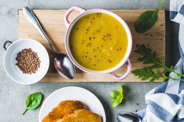 Vegetable cream soup in a pink bowl and ingredients on a grey concrete background