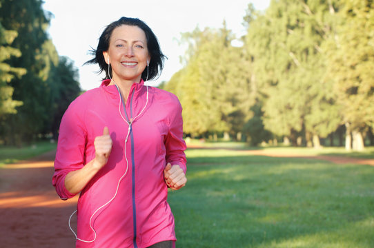 Portrait of elderly woman running with headphones in the park