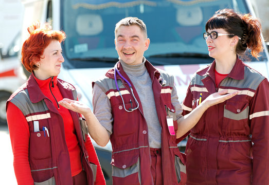 Happy doctor man gesturing with smiling paramedics coworker colleague on ambulance vehicle background