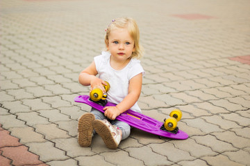 A blonde little girl is resting after a trip on a skateboard.