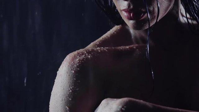 close-up. part of the face and shoulder of the girl athletes. she stands in the rain at night without clothing covering her breast with hand. the skin flowing stream of water