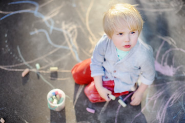 Naklejka premium Happy little kid boy drawing with colored chalk on asphalt.