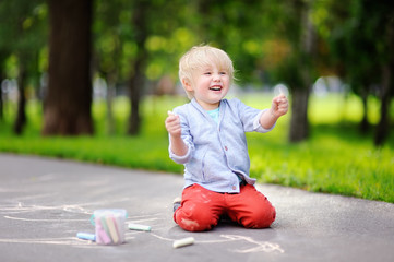 Happy little kid boy drawing with colored chalk on asphalt.