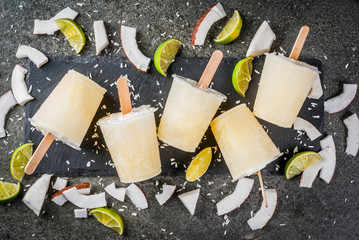 Summer desserts. Vegan diet food. Coconut and lime home fruit ice cream popsicles on a stick. On black stone table, copy space top view