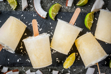 Summer desserts. Vegan diet food. Coconut and lime home fruit ice cream popsicles on a stick. On black stone table, copy space top view