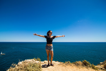 Beautiful latin woman standing on a rock above the ocean and welcomes the summer