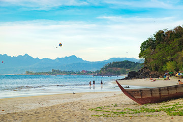Fototapeta na wymiar Seascape with islands on the horizon, old wooden fishing boat on the beach in the foreground. Paragliders at sunny day, summer adventure in Pantai Tengah Beach