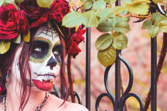 Close up portrait beautiful girl in makeup traditional Mexican Calavera sugar skull on the background of an iron fence with spikes. Day of the dead. Halloween celebration.