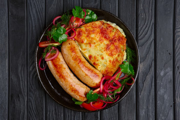 Fried homemade sausage with fried mashed potato, pickled onion and tomato