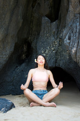 Girl practicing yoga in the shade of a beach cave