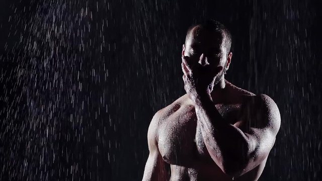 silhouette of a large muscular man bodybuilder in a dark room on top of flowing water breaks on the beautiful male body. dark background