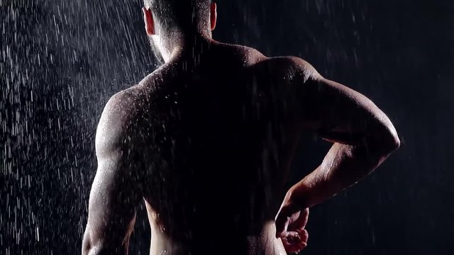 shooting from the back. posing big men athlete with the expansion of the widest back muscles and strain of the triceps . strong muscular man in the rain at night