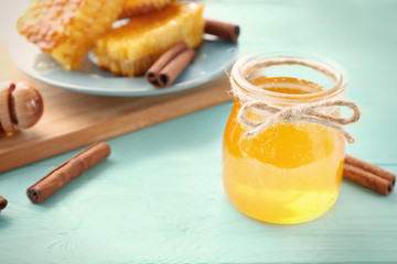 Glass jar with honey and cinnamon on color wooden table
