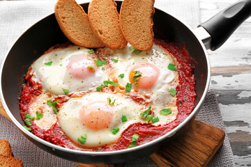 Frying pan with eggs in purgatory on wooden background