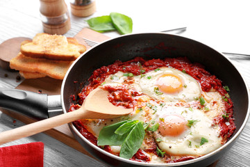 Frying pan with eggs in purgatory on wooden background
