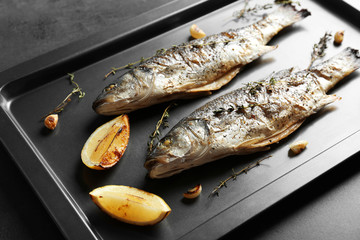 Baking sheet with fried fish on dark background