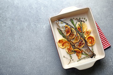 Baking dish with tasty fish, herbs and lemon on grey table