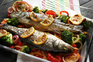 Baking dish with two tasty fish and garnish on grey background