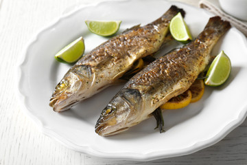 Two baked fish with lime and lemon on white plate