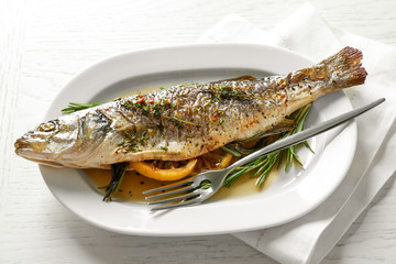 White plate with baked fish, lemon and herbs on table