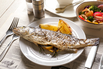 White plate with baked fish, lemon and herbs on table