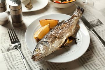 White plate with baked fish, lemon and herbs on table