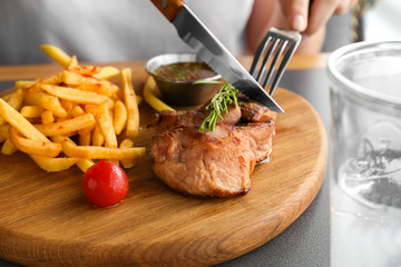 Woman eating steak with fork and knife on wooden board at restaurant