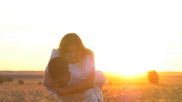 Young beautiful couple girl and boy playing and flirting in a wheat field at sunset. The guy is holding the girl on her back