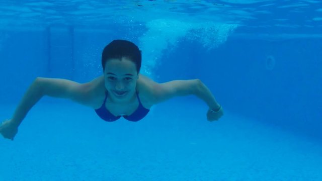 Girl in the pool under the water. The girl is wearing glasses under the water.