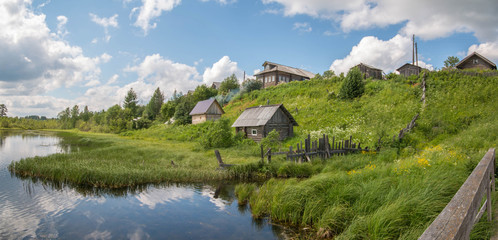 North Russian village. Summer day, river, old cottages on coast.