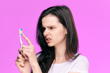Beautiful young woman on a pink background holds a toothbrush
