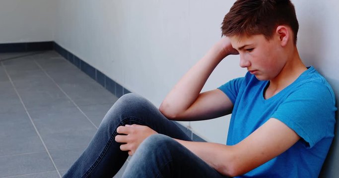 Sad schoolboy sitting in corridor