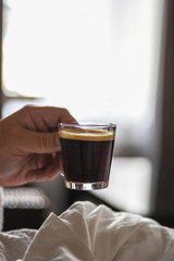 woman holding a small glass of cappuccino in early morning light