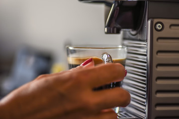 woman holding glass cup under cappuccino maker in early morning