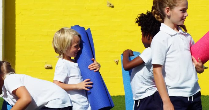 School kids holding yoga mat and interacting with each other