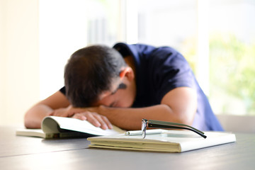 Young man sleeping on the table with book opened, weary & tired of reading (studying)