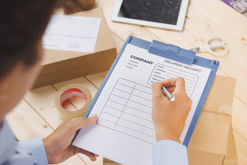 Close-up of deliveryman making notes in delivery receipt at table