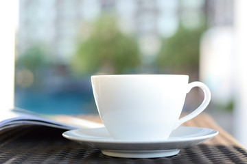 Coffee cup with book on the table in blurred building & green plant background - chill out in resort or hotel concept