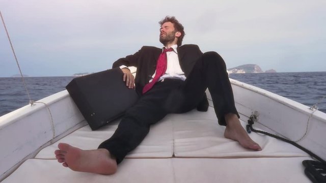 Desperate man in suit with a briefcase sitting on the prow of a boat in the middle of the ocean