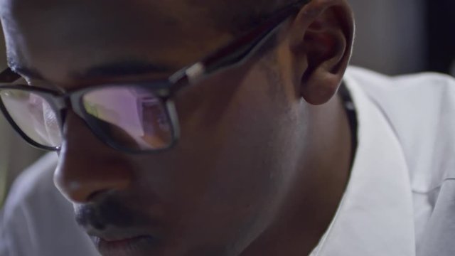 Closeup of face of concentrated African man with reflection of computer screen in eyeglasses